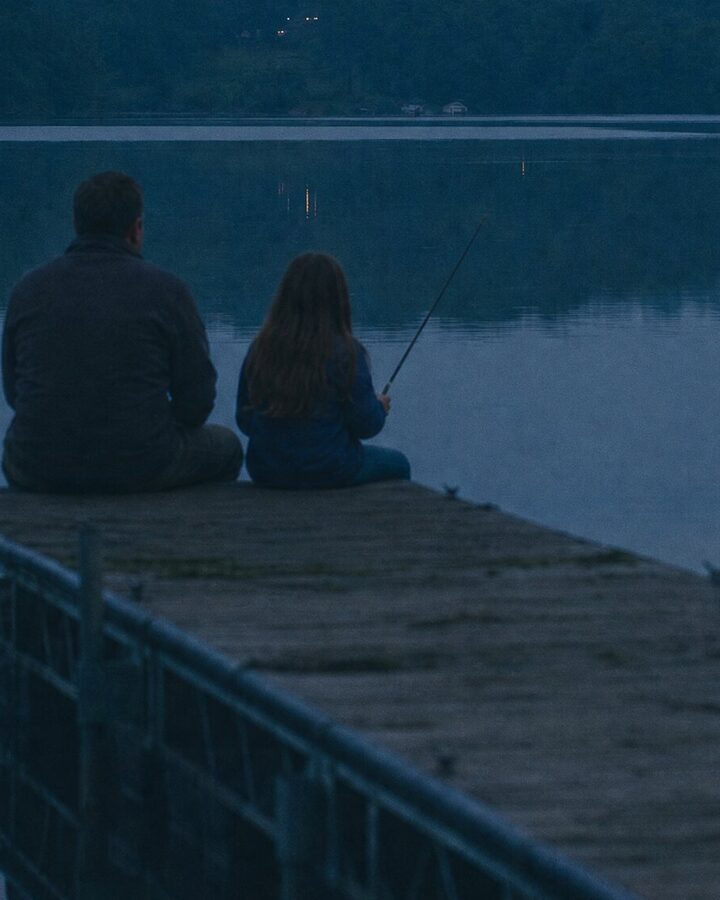 A father and daughter fishing from the Lake Logan dock at dusk